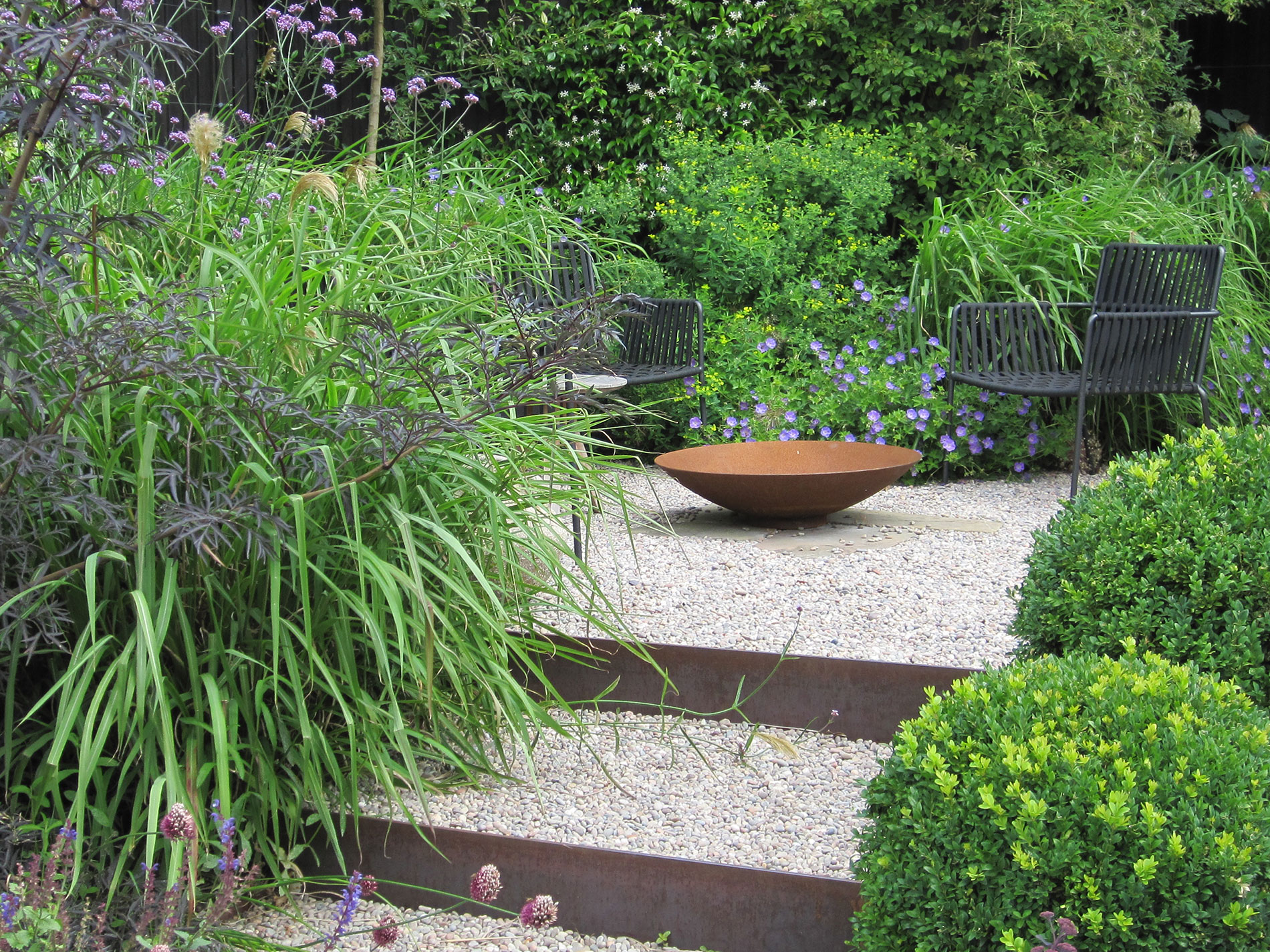 Small steel step risers create contain gravel steps rising to a gravel seating area.